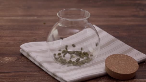 Semillas de calabaza peladas ecológicas se vierten en una jarra de vidrio — Vídeo de stock