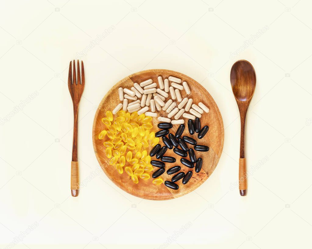Health care composition with different kind of natural vitamin and supplement capsules on a wooden plate with wooden fork and spoon. Immunity boosting capsules. Biologically active additives