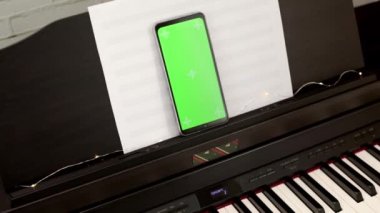 Elektronik piyanoda yeşil ekranlı akıllı telefon. Piyano dersi online. Online müzik bayramı konseri ya da konferans. Mobil müzik uygulamaları için bir model. Online müzik eğitimi. Yavaş çekim