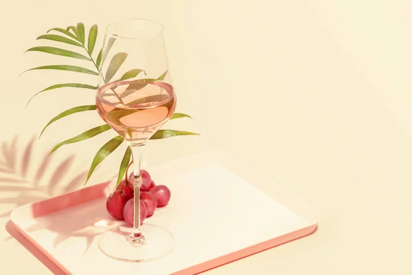 Pembe arka planda palmiye yaprağı ve üzüm ile bir bardak gül şarabı.