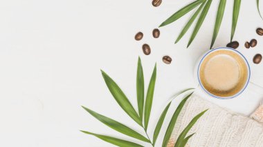 Seçici odak, İskandinav tarzı rahat ev kompozisyonu bir fincan kahve, örgü süveter, palmiye yaprakları, beyaz arka planda kahve çekirdekleri ve fotokopi alanı. Sıcak bir sabah, evde dinleniyorum. Lagom