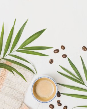 Sıcak bir sabah, evde dinleniyorum. Seçici odak, İskandinav tarzı rahat ev kompozisyonu bir fincan kahve, örgü süveter, palmiye yaprakları, beyaz arka planda kahve çekirdekleri ve fotokopi alanı. Lagom