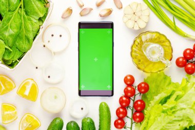 Organic vegetables and smartphone with green screen on a white background. The concept of online purchases of farm vegetables, fruits and greens. Mock up suitable for mobile apps for recipes, diets