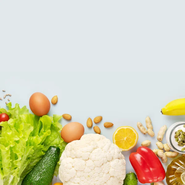 Keto diyet kompozisyonu organik sebzeler ve meyveler, zeytinyağı, fındık, tohum ve yumurtalar ile mavi bir zemin üzerinde fotokopi alanı ile. Sağlıklı gıda kavramı. Bol vitamin ve besin içeren yiyecekler.