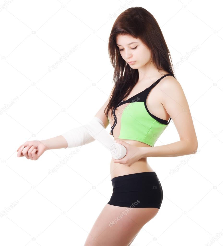 Young girl in a sports tank top and shorts is bandaging his arm with an elastic bandage