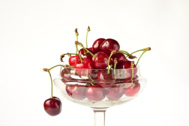 beyaz zemin üzerinde bir cam kap içinde olgun kırmızı kiraz