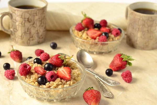 Gachas con granos, bayas frescas en un tazón de vidrio y té para el desayuno —  Fotos de Stock