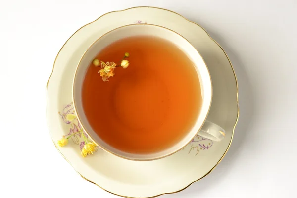 Beyaz arka planda ıhlamur çiçekleri olan bir fincan çay.