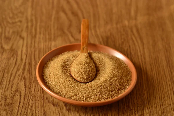Brown sugar in a wooden spoon on a plate — Stock Photo, Image
