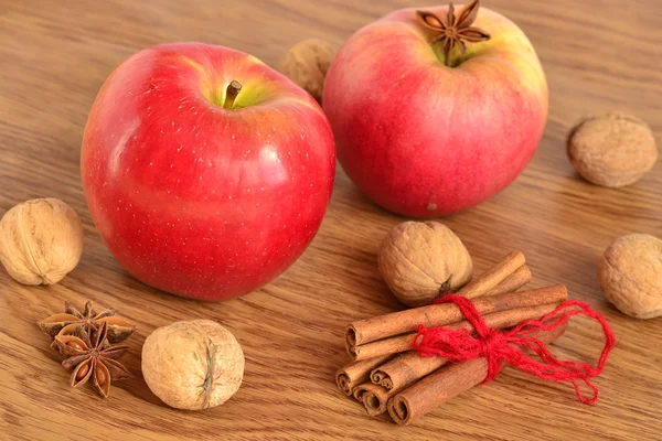 Red apple, walnuts, cinnamon and star anise on a wooden background — Stock Photo, Image