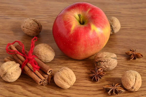 Red apple, walnuts, cinnamon and star anise on a wooden background — Stock Photo, Image