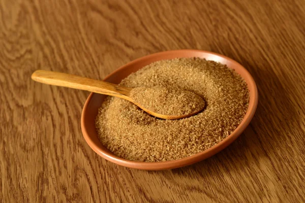 Bruine suiker in een houten lepel op een plaat — Stockfoto