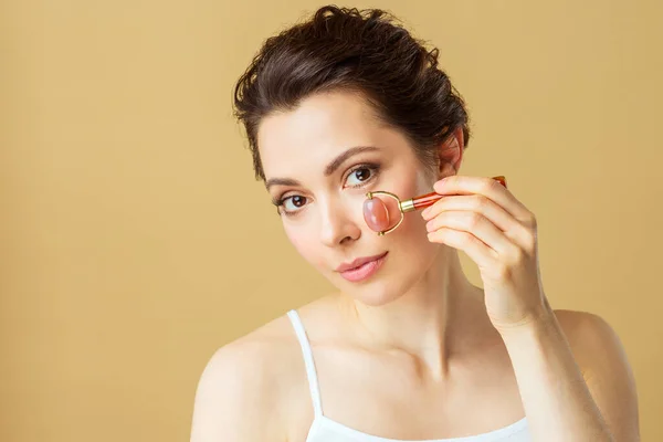 Retrato de una mujer joven usando un rodillo de masaje facial hecho de cuarzo rosa natural — Foto de Stock