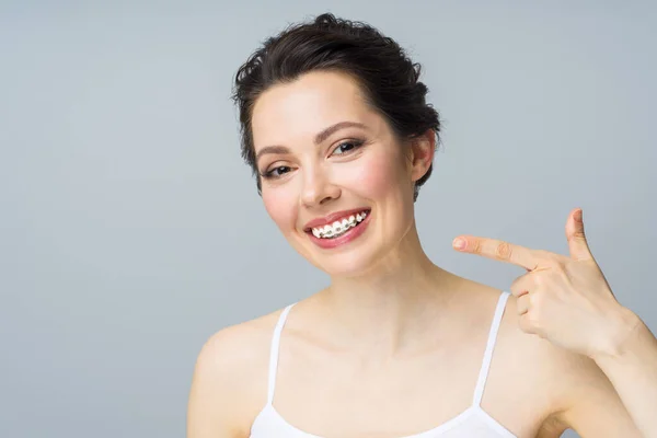 Mladá žena s rovnátky na zubech, usmívá se a ukazuje rukou na kopírovací prostor. — Stock fotografie