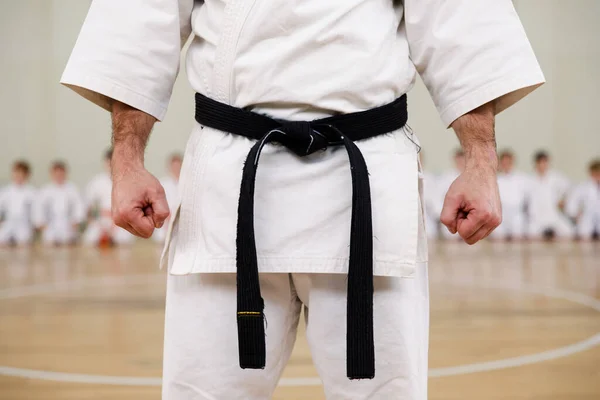 Maestro di karate in kimono bianco e con cintura nera, si trova di fronte alla formazione dei suoi studenti. Scuola di arti marziali in allenamento in palestra. — Foto Stock