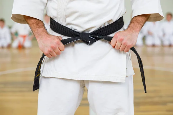 Maestro di karate in kimono bianco e con cintura nera, si trova di fronte alla formazione dei suoi studenti. Scuola di arti marziali in allenamento in palestra. — Foto Stock