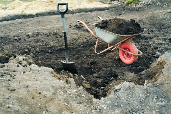 Trabajar con herramientas de jardín, pala y carretilla en el sitio de una casa de campo. Preparación para los trabajos de construcción. —  Fotos de Stock