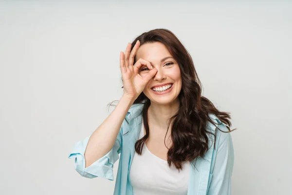 Retrato de una mujer sonriente mostrando un signo OK y mirando a una cámara aislada sobre un fondo blanco. — Foto de Stock