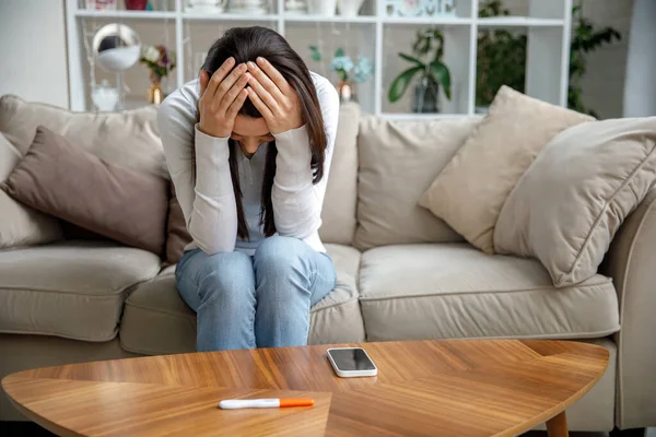 Üzgün genç bir kadın elinde hamilelik testi tutuyor. İstenmeyen hamilelik kavramı.