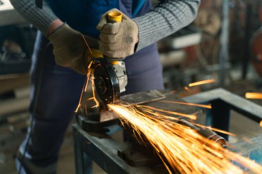 Özel kıyafet ve gözlüklü bir çilingir üretim işinde çalışıyor. Açı öğütücüyle metal işleme. Metal işçiliğinde kıvılcımlar