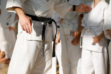 Beyaz kimonolu ve siyah kuşaklı bir karate ustası öğrencilerinin önünde duruyor. Dövüş sanatları okulu spor salonunda eğitim görüyor..