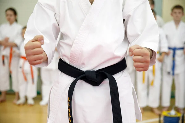 Karate-Meister im weißen Kimono und mit schwarzem Gürtel steht vor der Formation seiner Schüler. Kampfsportschule im Training in der Turnhalle. — Stockfoto