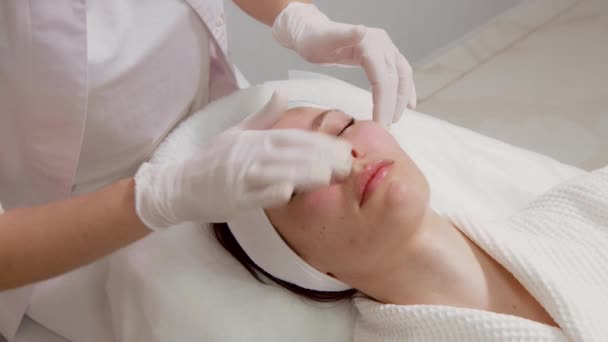 A specialist gives a facial massage to a young woman. Cosmetic procedure for facial skin care. Cosmetology clinic services — Stock Video