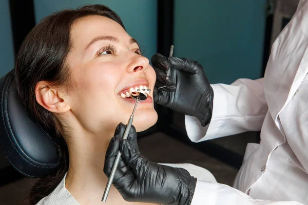 En ung kvinna på en tandklinik med en tandläkare. Kvinnan med tandställning ler. Begreppet friska tänder. — Stockfoto