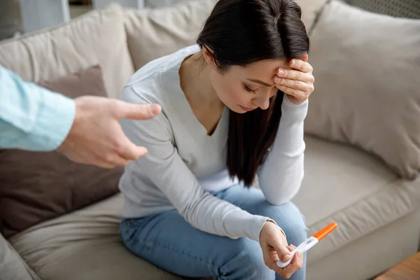 A sad young woman holds a pregnancy test in her hand. The concept of unwanted pregnancy. — Stock Photo, Image