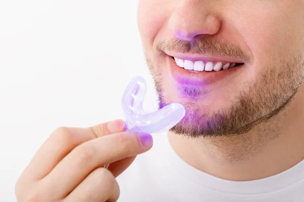 Un hombre sostiene en su mano una lámpara ultravioleta para blanquear los dientes en casa. Una sonrisa blanca como la nieve después del blanqueamiento. — Foto de Stock