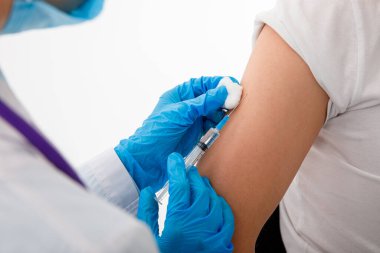 Tıbbi maskeli hastaya iğne yapmadan önce elinde şırınga tutan doktor. Covid-19 ya da koronavirüs aşısı. Kapat.
