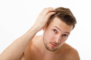 Genç bir adam aynada kendine bakar, saçları erkenden dökülmeye başlar..