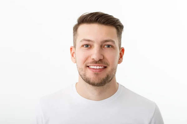 Retrato de un joven alegre con una camiseta blanca sobre un fondo blanco. El tipo está de pie mirando a la cámara y sonriendo. Imagen De Stock