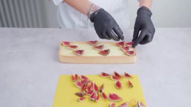 Baker, üzerine incir dilimleri koyarak kare bisküvi süslüyor.