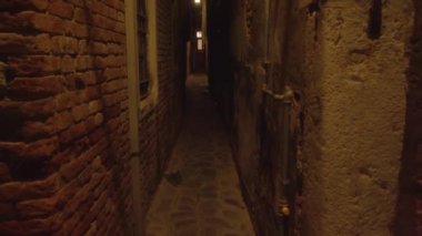 Venedik 'in eski tuğlaları ve yıkılmış binaları arasında Venedik' in aydınlık yollarıyla aydınlanan uzun karanlık dar geçidi.