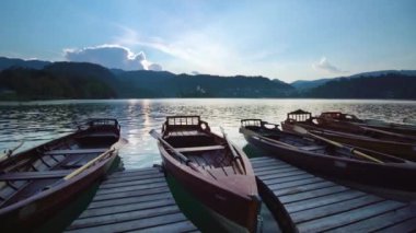 Bled Gölü 'nde günbatımında küreklerle demirli ahşap kayıklar.