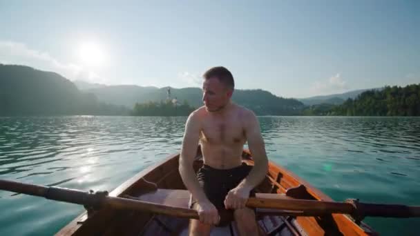 Νεαρός άνδρας κάθεται με βάρκα πλέοντας προς το μικρό νησί στη λίμνη Bled — Αρχείο Βίντεο