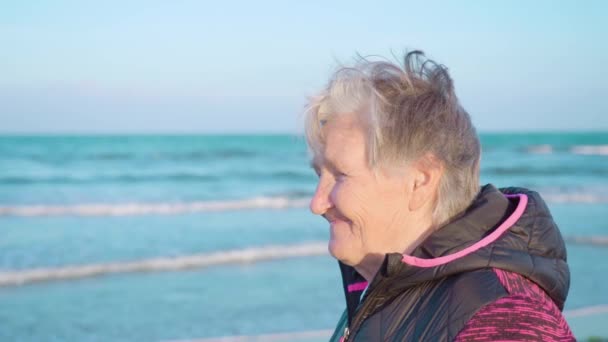 Öreg nő a haj integetett a szél élvezi a tengerre néző tengerparton — Stock videók