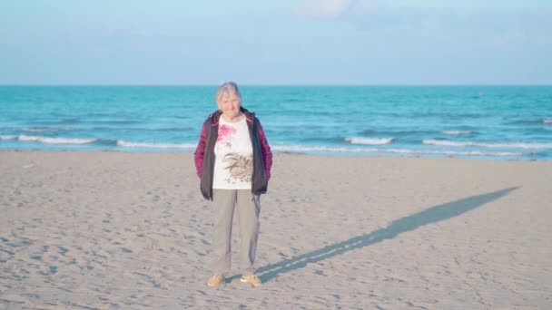 Oudere vrouw staat op zee strand tegen golven bij zonsondergang — Stockvideo