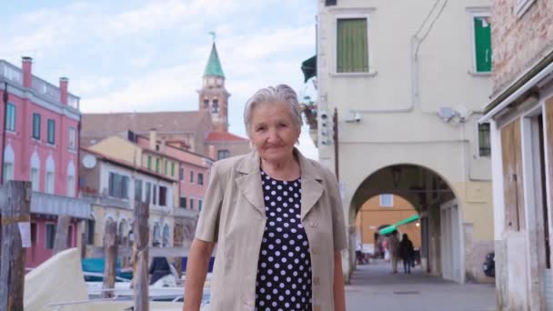Oude vrouw staat op kanaal dijk straat met huizen — Stockvideo