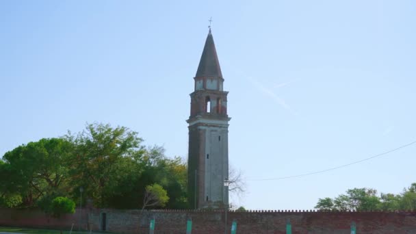 Iglesia campanario con valla de ladrillo se encuentra entre los árboles — Vídeos de Stock