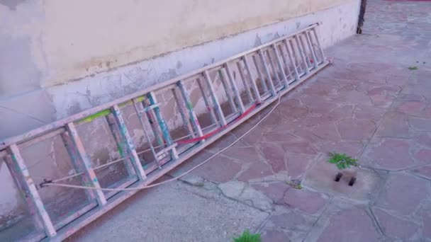 Старая лестница лежит на земле опираясь на стену здания — стоковое видео