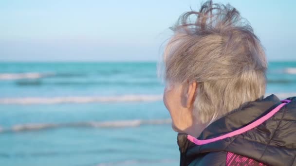 Пожилая женщина наслаждается качающимися морскими волнами, стоящими на пляже — стоковое видео