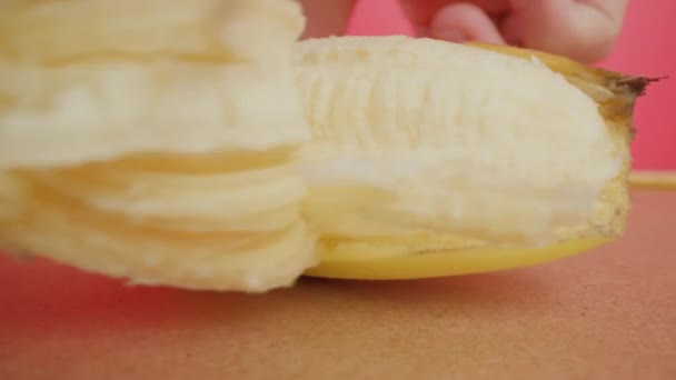 L'homme épluche lentement la peau jaune de banane contre le mur rose — Video