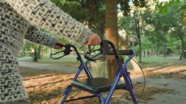 Yaşlı kambur kadın rollator aylakları kullanarak yürüyor