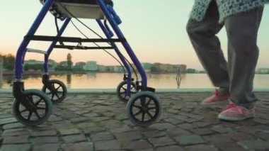 Yaşlı kadın, göl kıyısında yuvarlak bir aletle yürüyor.