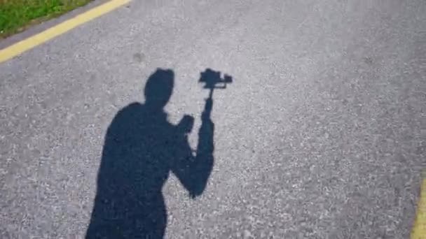 Operator cień przenosi filmowanie asfaltowej drogi w pobliżu trawy — Wideo stockowe