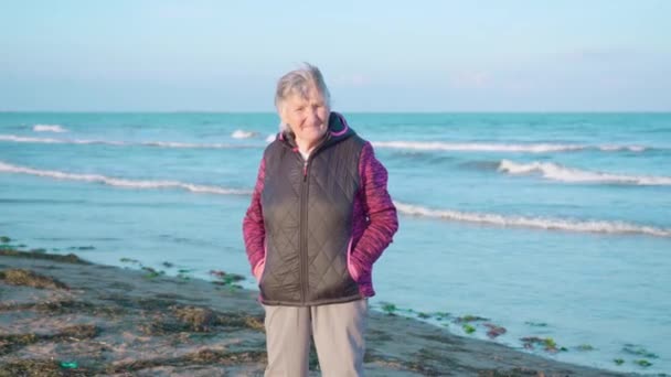 Idős nő áll a nedves homokos strandon élvezi az időjárás — Stock videók