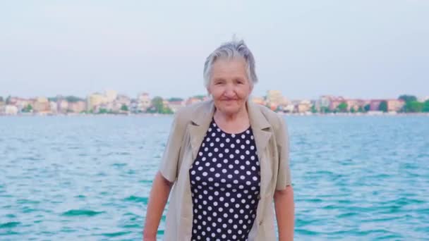 Anciana viajera pasea por la orilla sonriendo ampliamente — Vídeos de Stock