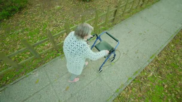 Hunched abuela paseos cerca de valla usando caminar marco — Vídeos de Stock